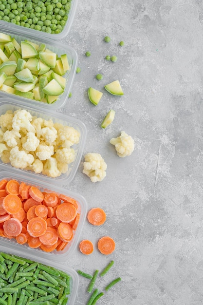 A variety of frozen vegetables in plastic containers on a gray\
concrete background copy space