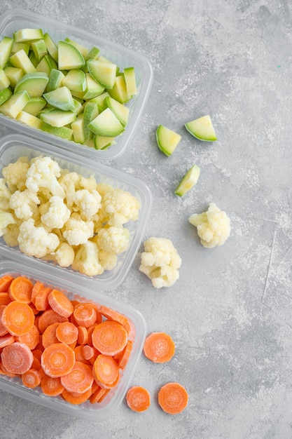 A variety of frozen vegetables in plastic containers on a gray\
concrete background copy space