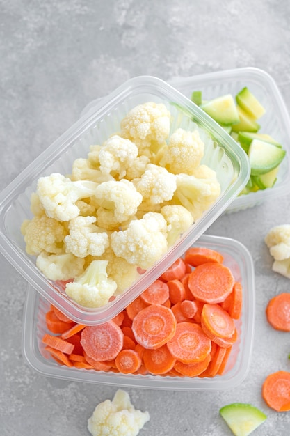 A variety of frozen vegetables in plastic containers on a gray concrete background Healthy food