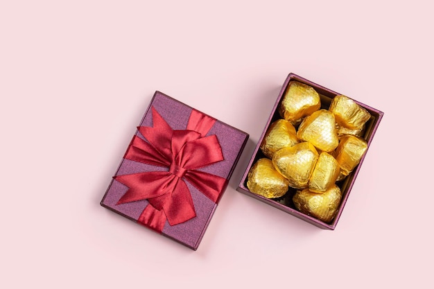 Variety of gifts and chocolates in the shape of a golden heart isolated pink background Valentine39s concept