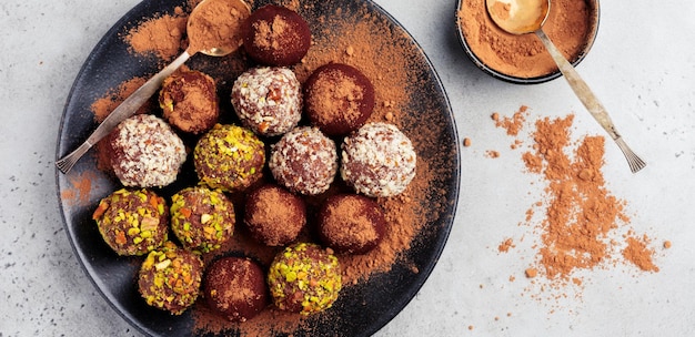 Variety of homemade dark chocolate truffles with cocoa powder, pistachios, almonds in light gray background texture. Top view, copy space.