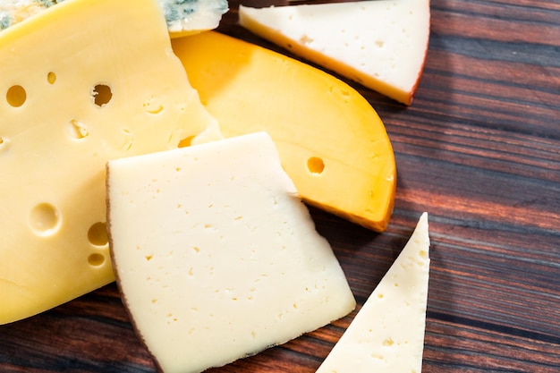 Variety of large gourmet cheese wedges on a dark wooden background.