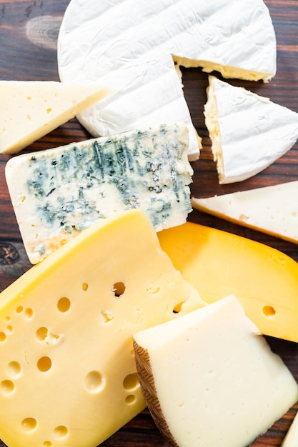 Variety of large gourmet cheese wedges on a dark wooden background.