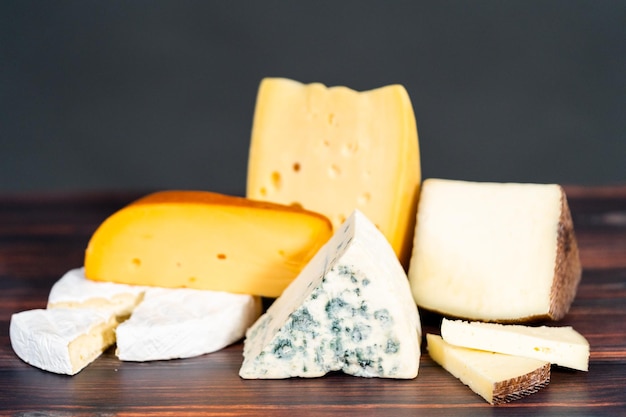 Variety of large gourmet cheese wedges on a dark wooden background.