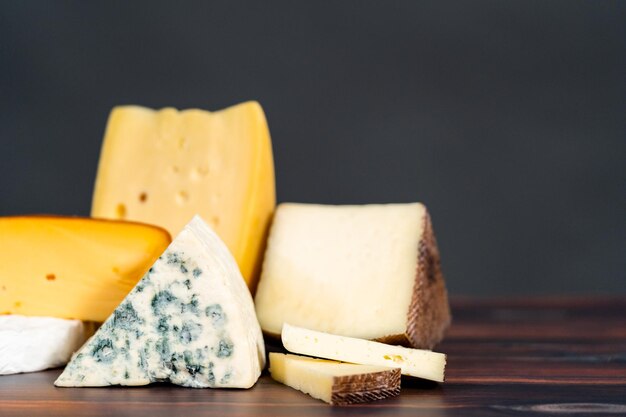 Varietà di grandi spicchi di formaggio gourmet su uno sfondo di legno scuro.