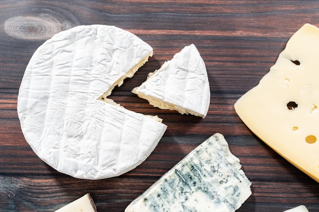 Variety of large gourmet cheese wedges on a dark wooden background.