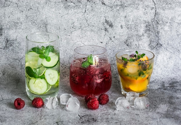 Variety of lemonade on a gray background Lemonade with raspberries peach fresh thyme and refreshing water with lime cucumber and mint