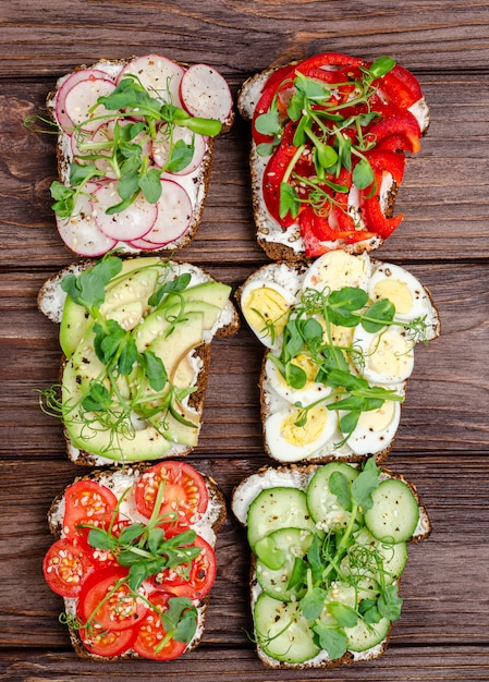 Variety of mini sandwiches with cream cheese and vegetables on a wooden surface