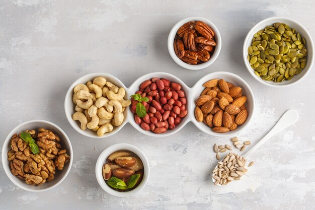 Photo a variety of nuts and seeds in a white bowls, top view, copy space, food background. healthy vegetarian food concept.