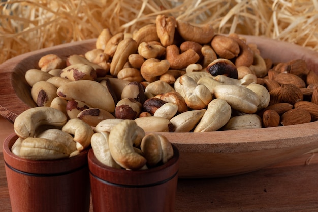 Variety of nuts  in a wooden bowl and in two wooden cups with straw background. Main nuts of Brazilian cuisine.