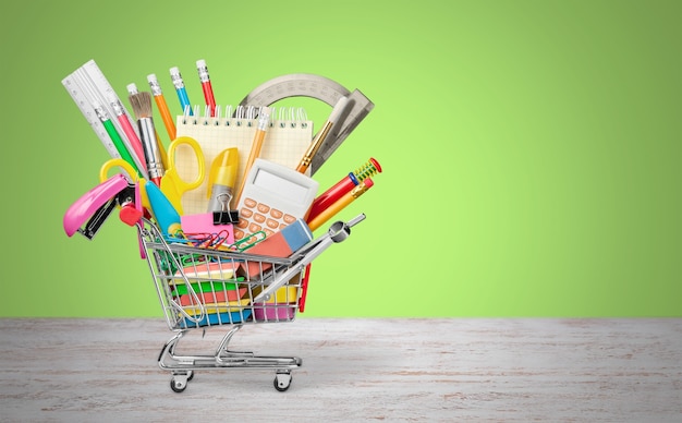 Variety office supplies in little shopping cart on wooden table  on background