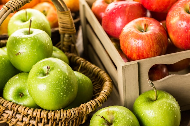 Variety of organic apples in baskets on wood table.