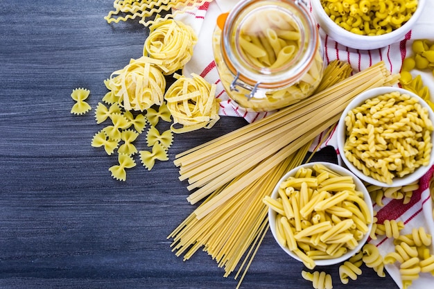 Variety of organic dry pasta on wood board.