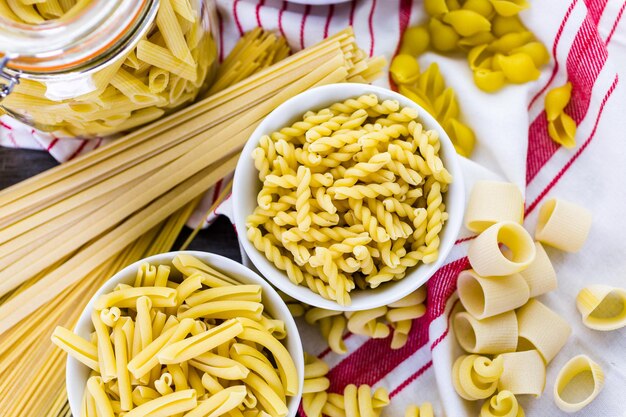 Variety of organic dry pasta on wood board.