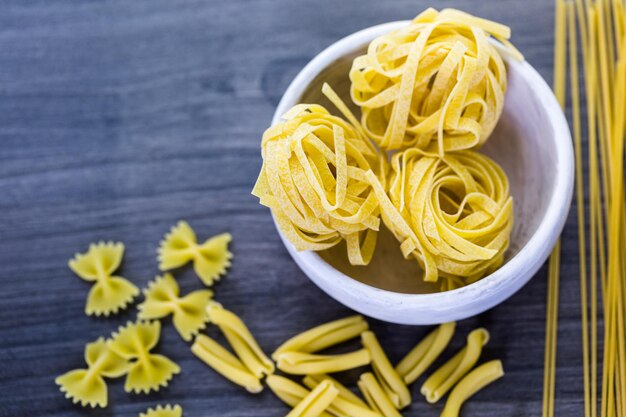 Variety of organic dry pasta on wood board.