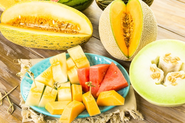 Photo variety of organic melons sliced on wood table.