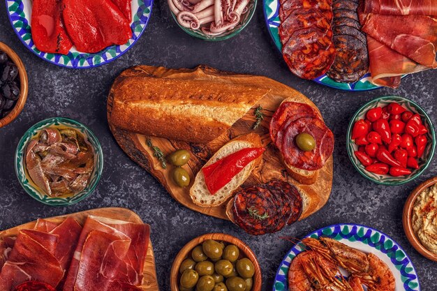 a variety of pieces of jamon, chorizo, salami, bowls with olives, peppers, shrimps, anchovies, chickpeas puree.