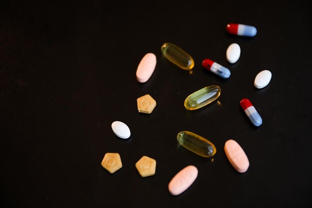 A variety of pills are scattered on a black background.