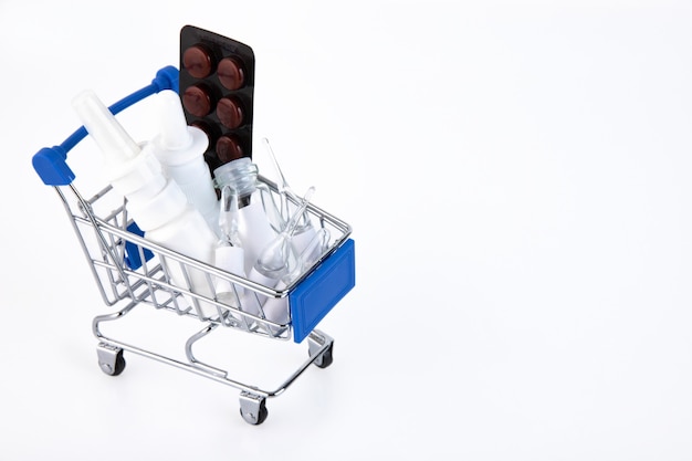 Variety of pills in blister packs in a mini shopping trolley on a white background