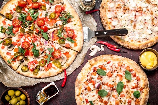 Variety of pizzas with sauces. On a rustic background.