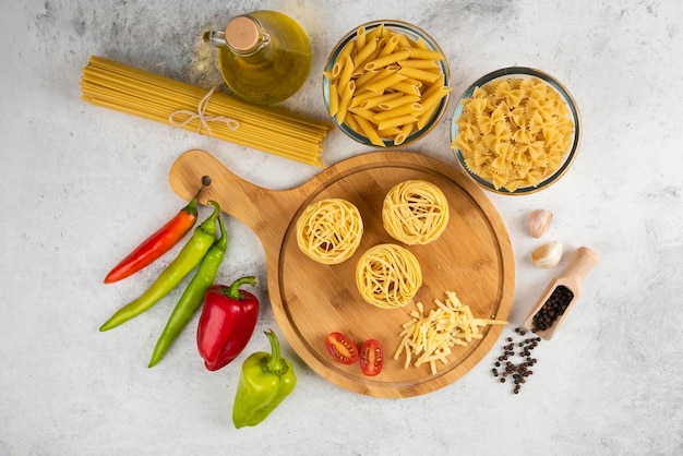 Variety of raw pasta oil and fresh vegetables on white table