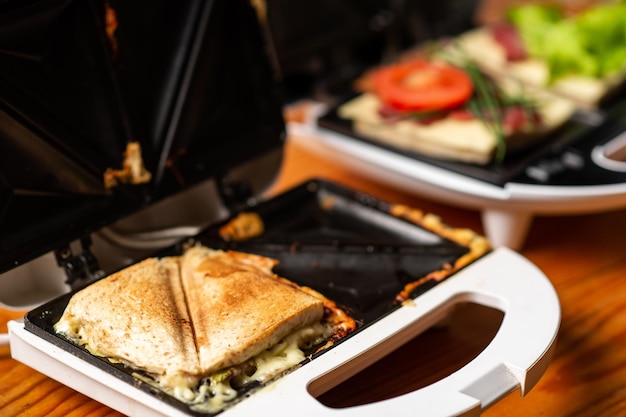 A variety of sandwiches that can be prepared in a sandwich maker concept Row of electric sandwich makers on a wooden background