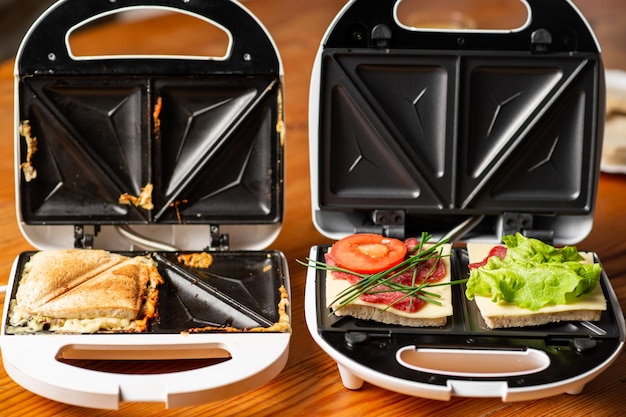 A variety of sandwiches that can be prepared in a sandwich maker concept Row of electric sandwich makers on a wooden background