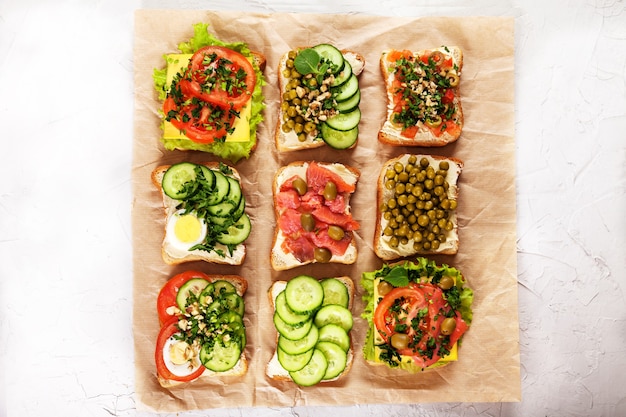 A variety of sandwiches with cream cheese, salmon, egg, herbs and vegetables on craft paper