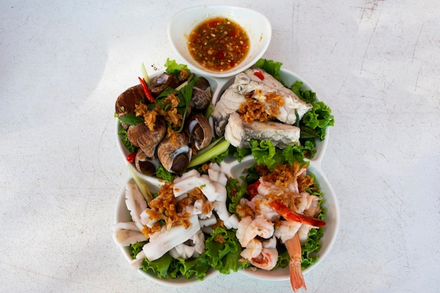 Variety seafood soft boiled served on vegetable and modern ceramic plate with spicy sour sauce for thai people guest customer eat drink on table at restaurant cafe shop in Pak Bara of Satun Thailand