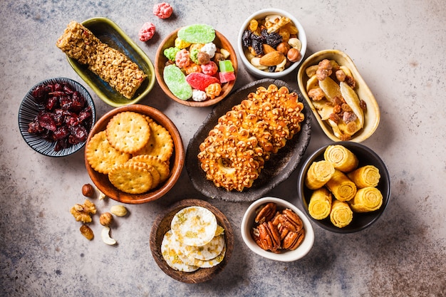 Variety of snacks and sweets on gray background. Waffles, nuts, sweets, cookies, chips and fruits, top view, flat lay.