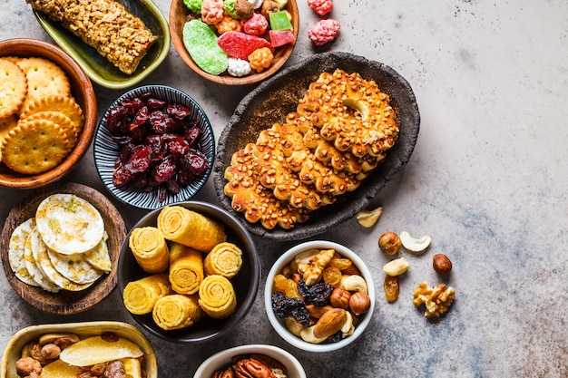 Varietà di snack e dolci su sfondo grigio. cialde, noci, dolci, biscotti, patatine e frutta, vista dall'alto.