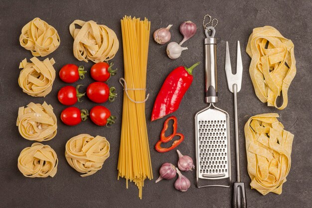 Variety of types and shapes of dry Italian pasta with tomatoes, red peppers, garlic, parsley. Grater and  fork