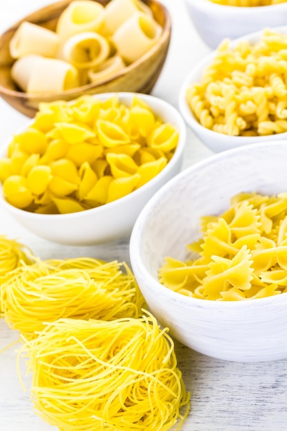 Variety of yellow dry pasta in small round bowls.