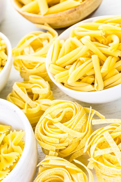 Variety of yellow dry pasta in small round bowls.