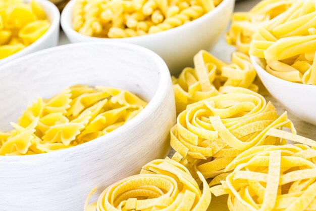Variety of yellow dry pasta in small round bowls.