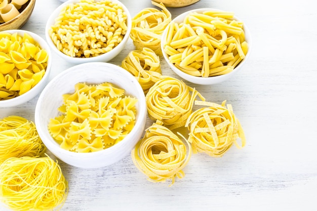 Variety of yellow dry pasta in small round bowls.