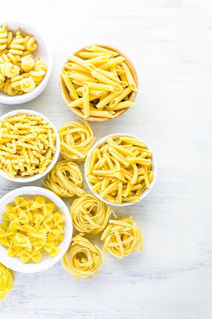 Variety of yellow dry pasta in small round bowls.