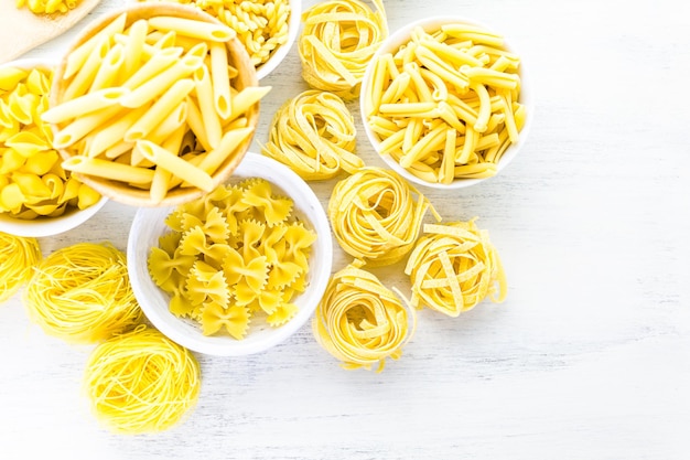 Variety of yellow dry pasta in small round bowls.