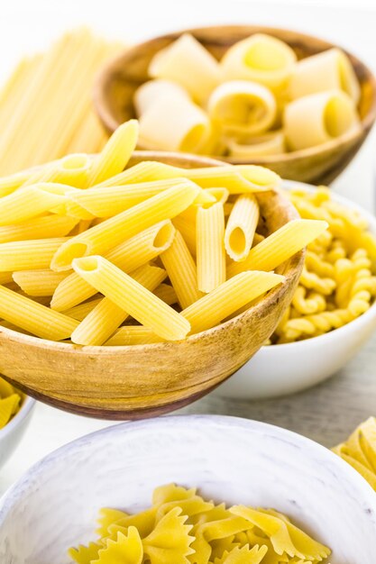 Variety of yellow dry pasta in small round bowls.