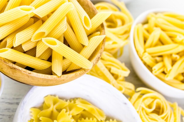 Variety of yellow dry pasta in small round bowls.