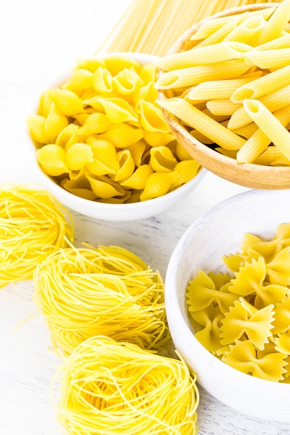 Variety of yellow dry pasta in small round bowls.