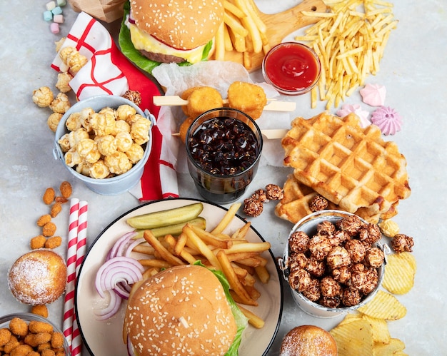 Various of american food French fries hamburgers nuggets hotdog chips popcorn sauces on a white background top view