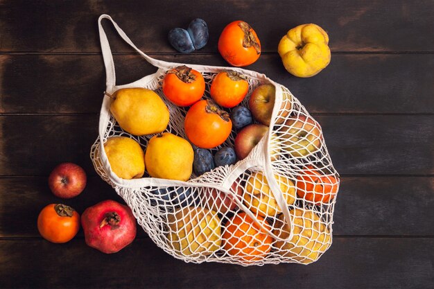 Various autumn fruits in a mesh bag on a dark wooden background.