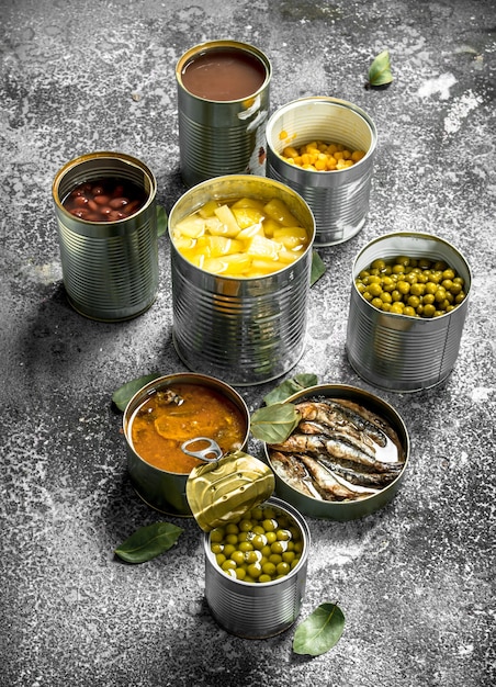 Various canned foods with meat, fish, vegetables and fruits in tin cans on rustic table.