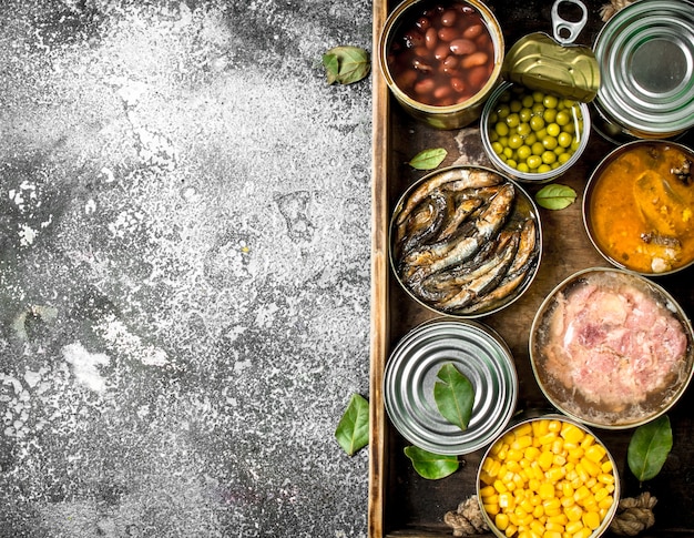 Various canned products in tin cans on a wooden tray on a rustic background