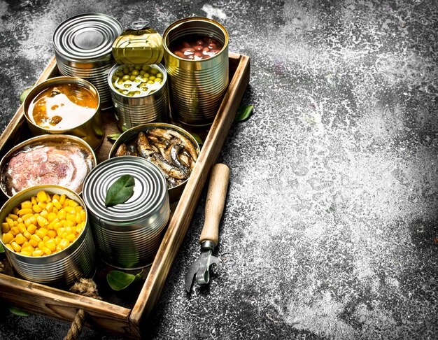 Various canned products in tin cans on a wooden tray on a rustic background