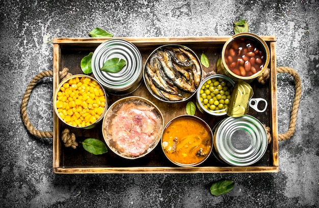 Various canned products in tin cans on a wooden tray on a rustic background