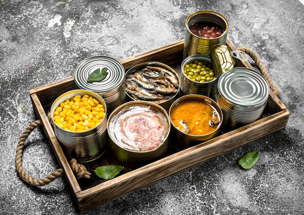 Various canned products in tin cans on wooden tray on rustic table.