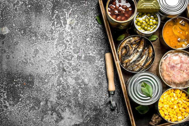 Various canned products in tin cans on wooden tray on rustic table.