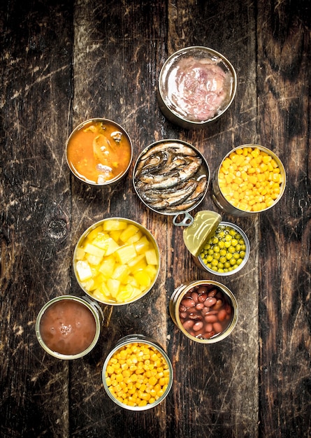 Various canned vegetables, meat, fish and fruits in tin cans on wooden table.